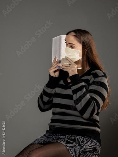 Happy world book day 2020, be safe and read to become someone else - woman covering face with book in mask while reading on grey studio background. Celebrating, education, art, protection concept. photo