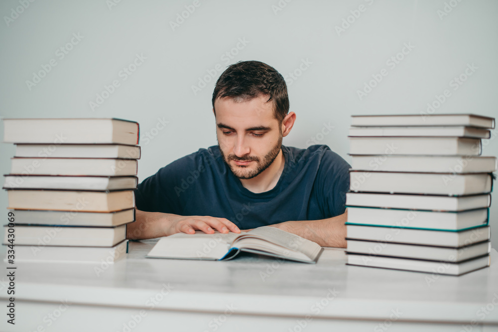 Young white European brunette man nerd in glasses teaches lessons, reads books, studied at university, prepares for exams, has many books at home in white backround table. Young white European brunette man nerd in glasses teaches lessons, reads books, studied at university, prepares for exams, has many books at home in white backround table.
