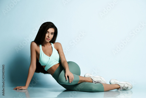 Beautiful sport brunette woman in sportswear working out doing stretching sports exercises in pastel green turquoise