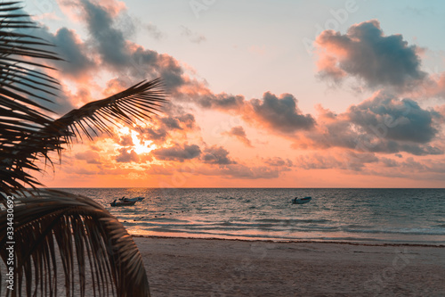 Palm leaves and fishing boats at sunrise on the sandy beach of the Caribbean
