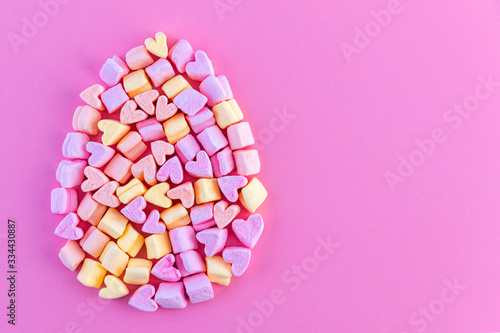 Marshmallows in the shape of colored hearts form the shape of an Easter egg. Concept. Pink background. Copy space