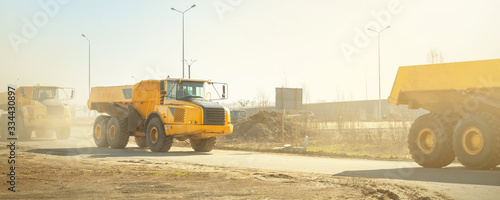 Many big articulated heavy industrial yellow dumper trucks driving on new highway road construction site on sunny day with blue sky background. Construction equipment machinery working on open pit photo