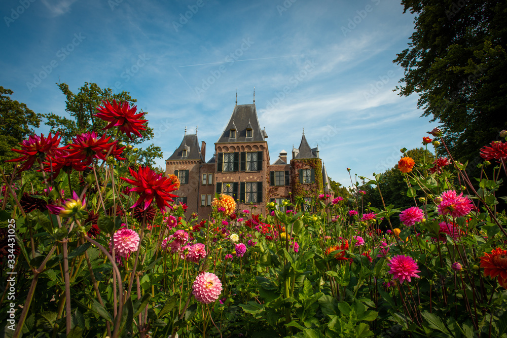 Garden with flowering dahlias in shades of orange and red in front of Keukenhof castle on a sunny day 