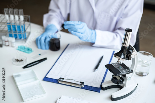 Scientist or medical in lab coat holding dropper with reagent, mixing reagents in glass flask, glassware containing chemical liquid, laboratory research and testing of Microscope