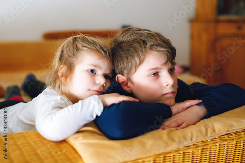 Cute little toddler girl and school kid boy watching animal movie or movie on tv. Happy healthy children, siblings during coronavirus quarantine staying at home. Brother and sister together.