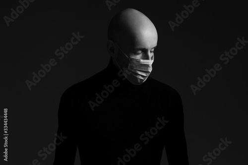 Coronavirus, Bio Protection Concept. Close up profile portrait of handsome bald man wearing medical mask, black turtleneck and praying. Copy-space. Monochrome studio shot