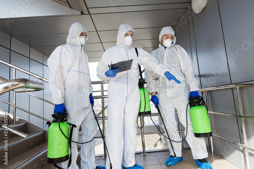 Men in protective suits deciding what to disinfect with spray