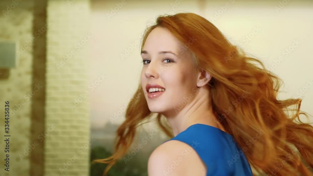 The beautiful sexy girl with red hair and playful look in the blue dress is spinning, smiling and looking at camera. Slowmo. The beautiful sexy girl with red hair and playful look in the blue dress is spinning, smiling and looking at camera. Slowmo.