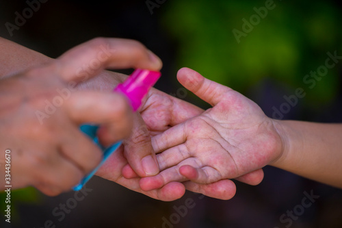 mother spry alcohol to cleaning her kids hand for hygiene protect weak ill chemotherapy, aids, kids patient from flu, germ, bacteria and virus covit-19 infection, in Blur background.