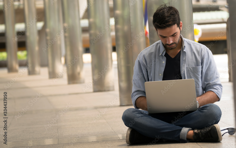 Portrait of young man sitting on the floor.Business man working with laptop.Happy young man working on laptop sitting at his working place outdoors.Successful business. Portrait of young man sitting on the floor.Business man working with laptop.Happy young man working on laptop sitting at his working place outdoors.Successful business.