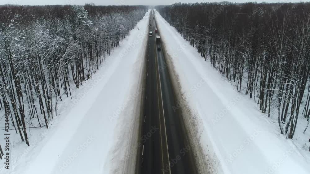 Aerial of cars and trucks driving in winter. Road surrounded by snow and trees. Aerial of cars and trucks driving in winter. Road surrounded by snow and trees.