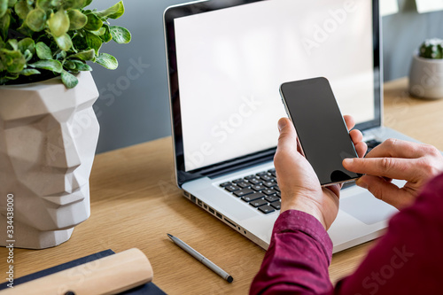 Close up of stylish composition with businessman, mock up laptop screen, cup of coffee, plants and office supplies in modern home office.