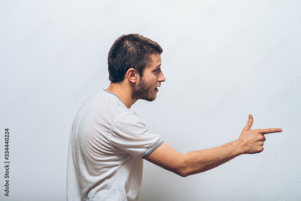 Closeup side view portrait of young man, pointing with finger at someone or something. Positive human face expressions, emotions, feelings, attitude, approach Closeup side view portrait of young man, pointing with finger at someone or something. Positive human face expressions, emotions, feelings, attitude, approach
