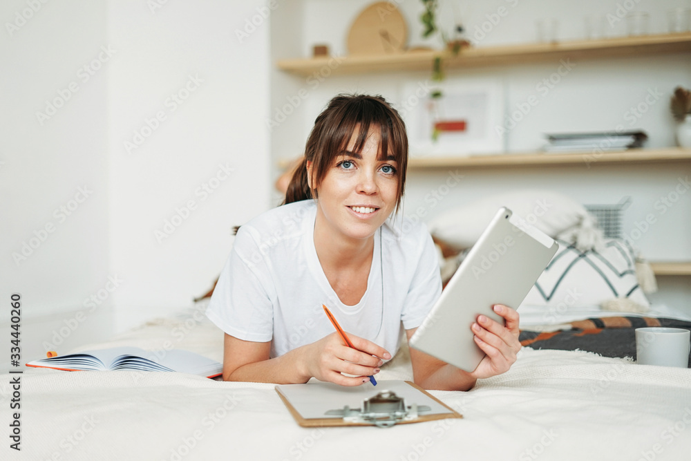 Working young brunette woman freelancer with tablet work on the bed at home in the bright interior Working young brunette woman freelancer with tablet work on the bed at home in the bright interior