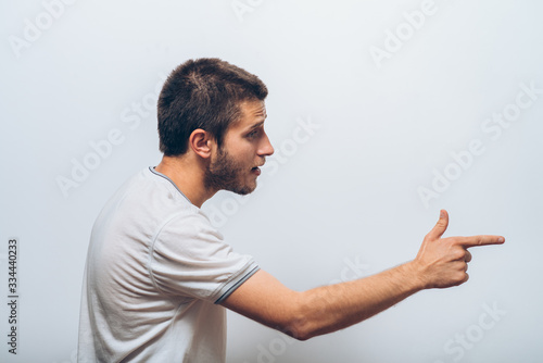 Closeup side view portrait of young man, pointing with finger at someone or something. Positive human face expressions, emotions, feelings, attitude, approach