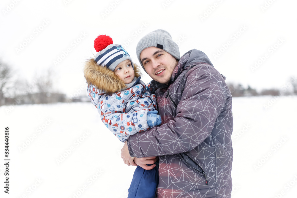 Happy dad holding his son, little funny kid boy on arm, on cold day, walking together in a park in spring, autumn or winter. Happy, joyful family.
