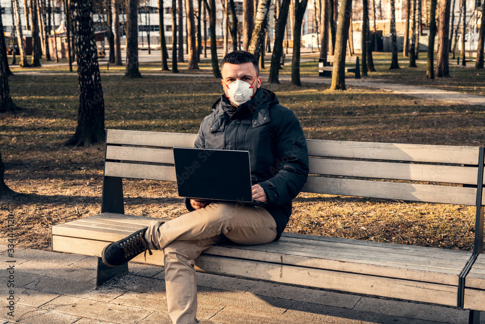 A man in a protective mask in an empty park. Quarantine and self-isolation.Working on a laptop in a park. Coronavirus pandemic. A man in a protective mask in an empty park. Quarantine and self-isolation.Working on a laptop in a park. Coronavirus pandemic.