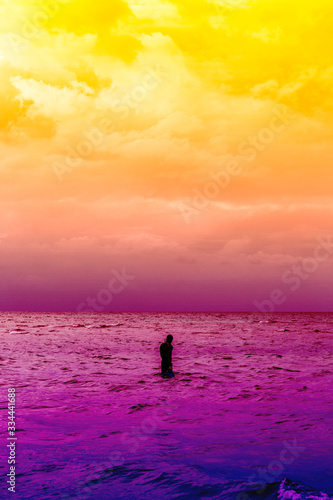 Abstract colorful cloudy sky and man walkingn into the sea