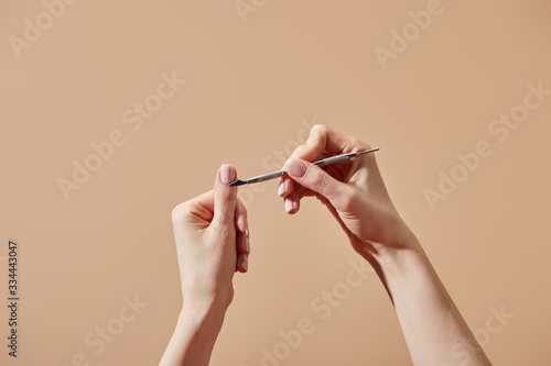 Cropped view of woman doing manicure using cuticle pusher isolated on beige