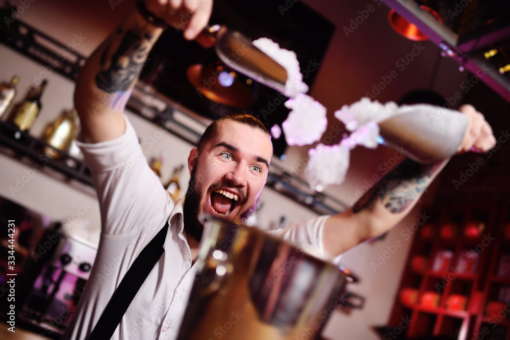 a handsome bearded bartender in a white shirt pours ice for cocktails and screams happily against the bar at a nightclub party