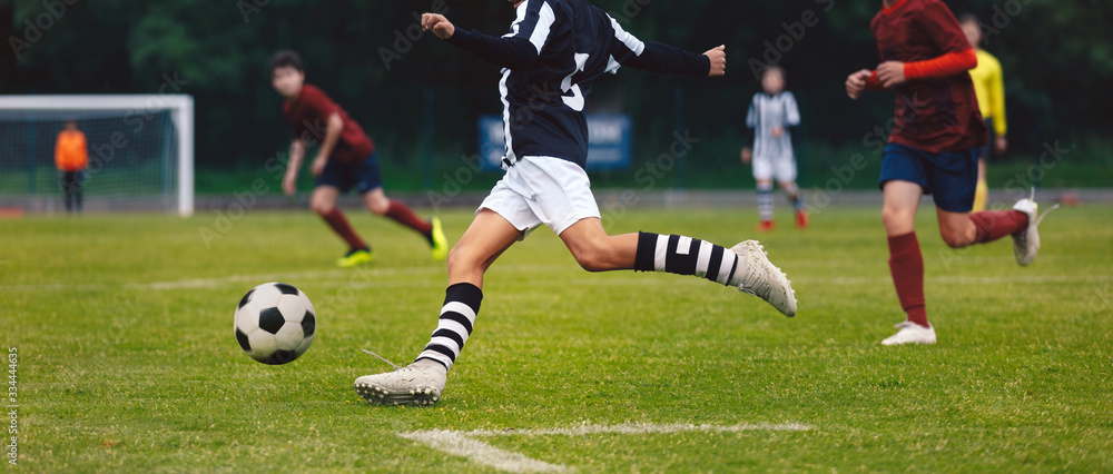 © matimix - Soccer player running and kicking ball on a game. Junior level footballers play football tournament match. Soccer competition between school boys teams