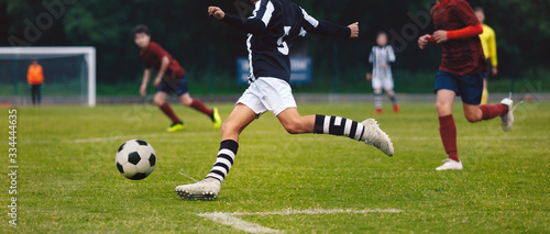 Fototapeta Naklejka Na Ścianę i Meble -  Soccer player running and kicking ball on a game. Junior level footballers play football tournament match. Soccer competition between school boys teams