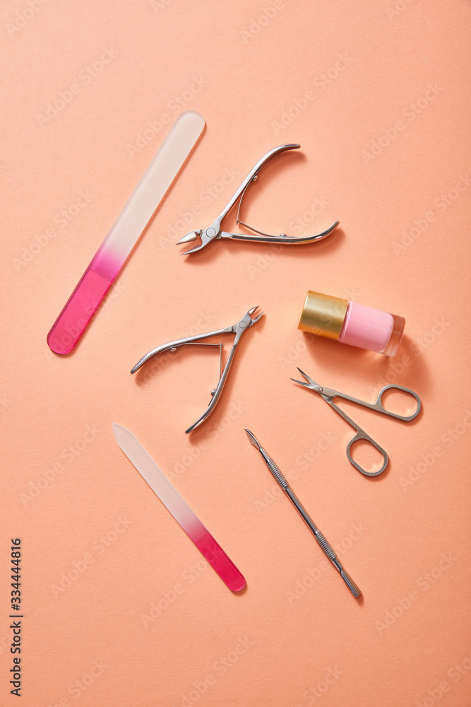 Top view of manicure instruments and bottle of pink nail polish on coral background Top view of manicure instruments and bottle of pink nail polish on coral background