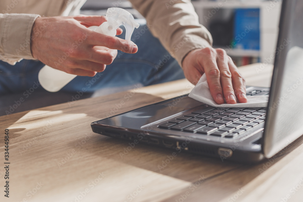 Man disinfects his laptop, cleaning keyboard. Wiping by rubbing alcohol