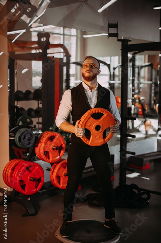 Stylish bearded athlete in a shirt and vest in the gym. holding a dumbbell