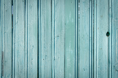 Background in grunge style. Wooden old fence with peeling paint. From vertical boards of turquoise color. With dark vignette around the edges.