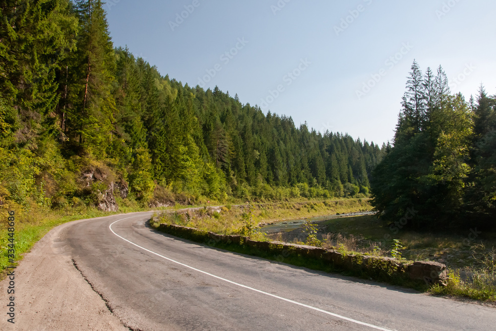 Empty road between fast river and mountains. Curve of the mountain road. Asphalt road in mountain in summer.  Landscape with empty road in mountain near the river.