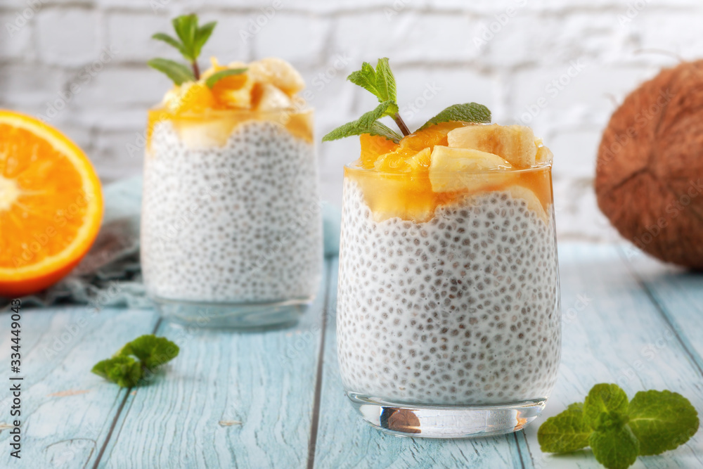Chia pudding with banana in two glass glasses with raw chia seeds on a blue wooden table Chia pudding with banana in two glass glasses with raw chia seeds on a blue wooden table