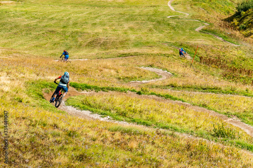 Eine Gruppe von Mountainbikern fährt über einen Single Trail einer Wiese kurvenreich abwärts