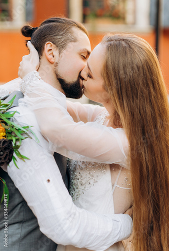 Portrait of a lovely young couple kissing each other in the yard against the backdrop of an orange building.