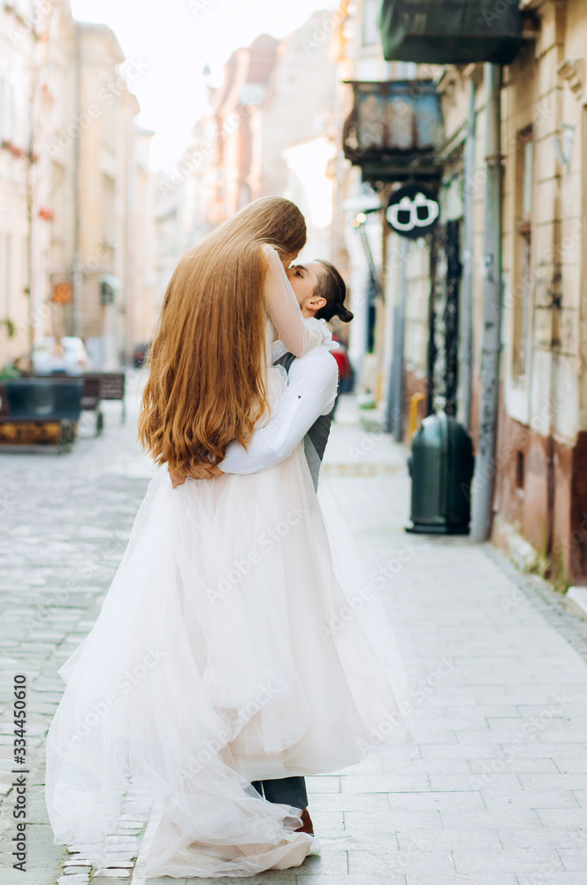 Handsome man holds his bride in hands on morning street background Handsome man holds his bride in hands on morning street background