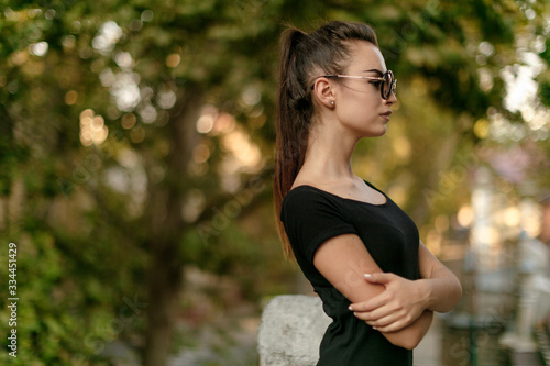 Portrait of a sensual girl, with sublime body, in black dress, hair gathered in a ponytail, posing in sunglasses, near the balcony. Horizontal view. Copy space.