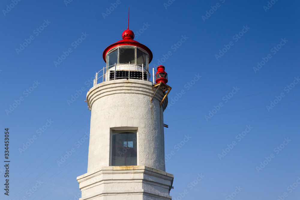 The white tower of the famous Tokarevsky lighthouse on the Egersheld peninsula in Vladivostok on a sunny day against a cloudless blue sky.