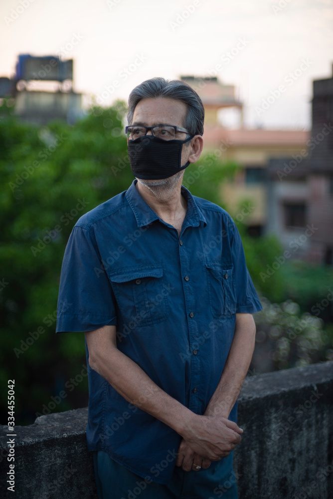 Portrait of an Indian old man wearing corona preventive mask on a rooftop in home isolation.Indian lifestyle, disease and home quarantine. Portrait of an Indian old man wearing corona preventive mask on a rooftop in home isolation.Indian lifestyle, disease and home quarantine.