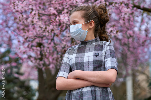 girl with a face mask is in the city outdoor, blooming trees, spring season, flowering time - concept of allergies and health protection from dusty air