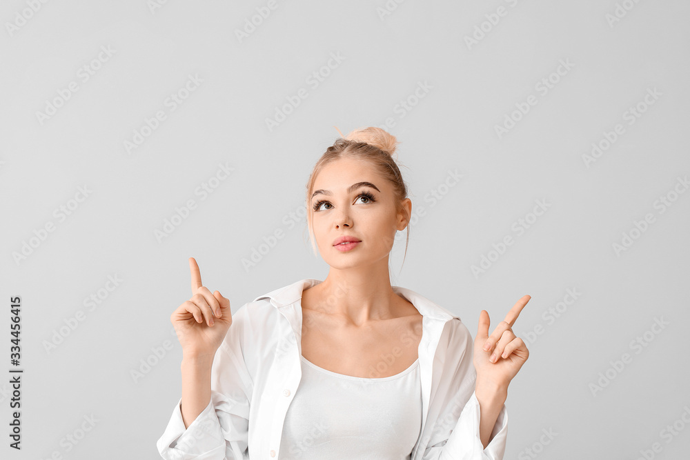 Beautiful young woman showing something on grey background Beautiful young woman showing something on grey background