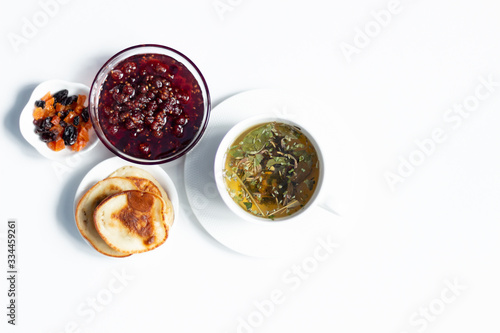 Fototapeta Naklejka Na Ścianę i Meble -  Herbal tea, raspberry jam, fritters, dry fruits on white background