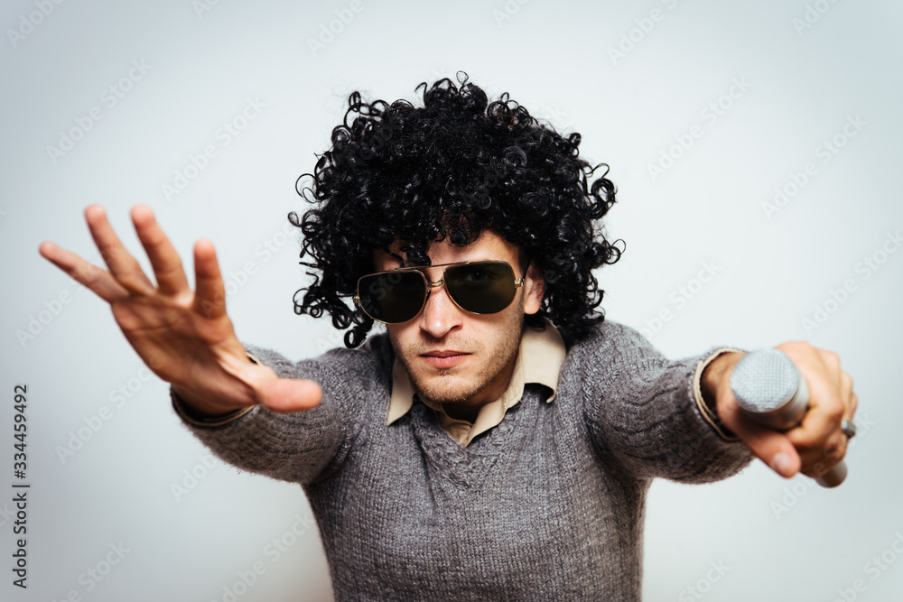A man in a wig, and sunglasses singing into a microphone. A man in a wig, and sunglasses singing into a microphone.