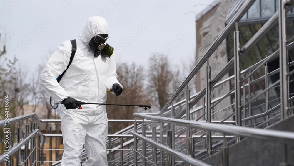 Sanitizer disinfects railing touch surfaces on coronavirus covid-19 quarantine with antibacterial sprayer. Worker in gas mask and hazmat protective suit cleans handrails in city public place. Sanitizer disinfects railing touch surfaces on coronavirus covid-19 quarantine with antibacterial sprayer. Worker in gas mask and hazmat protective suit cleans handrails in city public place.