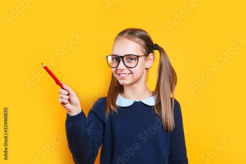 Fototapeta Naklejka Na Ścianę i Meble -  Schoolgirl in glasses pointing pencil at empty space for text.