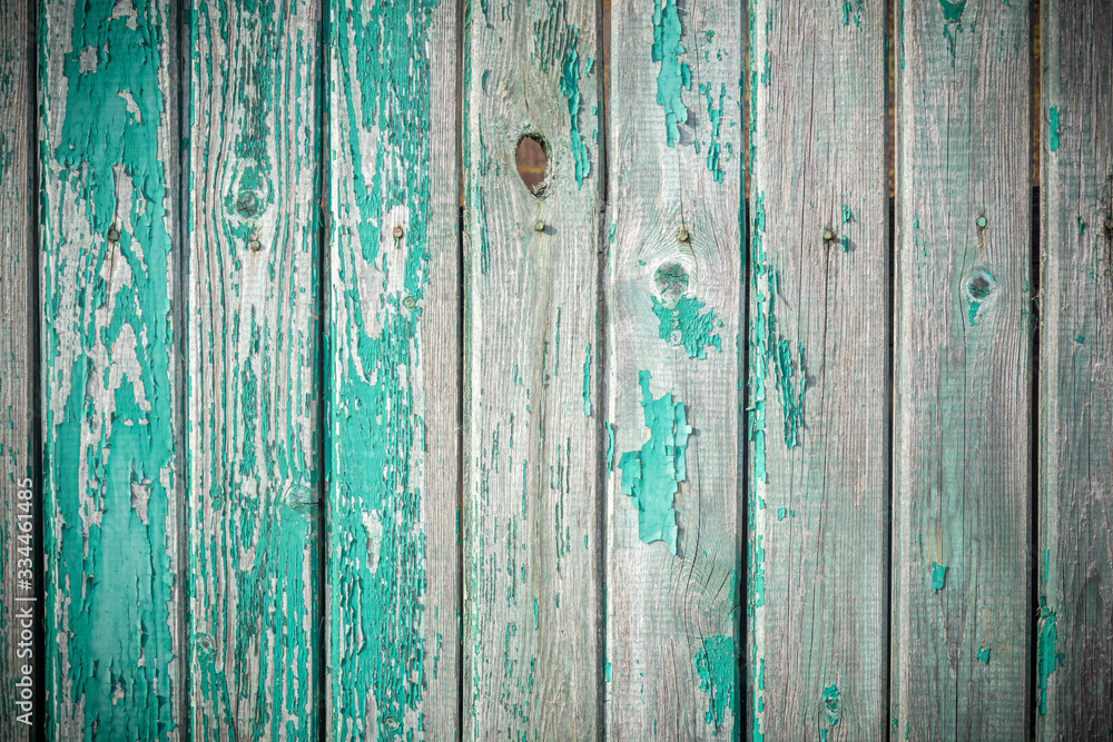 Background in grunge style. Wooden old fence with peeling paint. From vertical boards of turquoise color. With dark vignette around the edges. Background in grunge style. Wooden old fence with peeling paint. From vertical boards of turquoise color. With dark vignette around the edges.