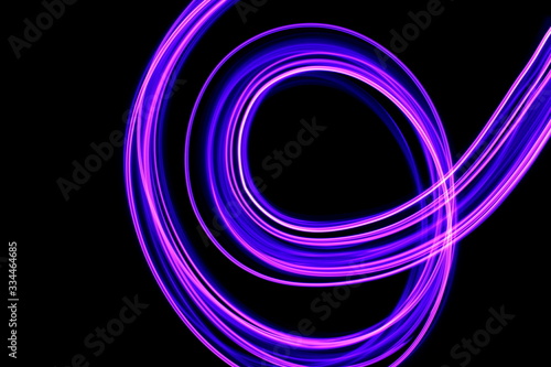 Long exposure photograph of neon purple streaks of light in an abstract swirl  parallel lines pattern against a black background. Light painting photography.