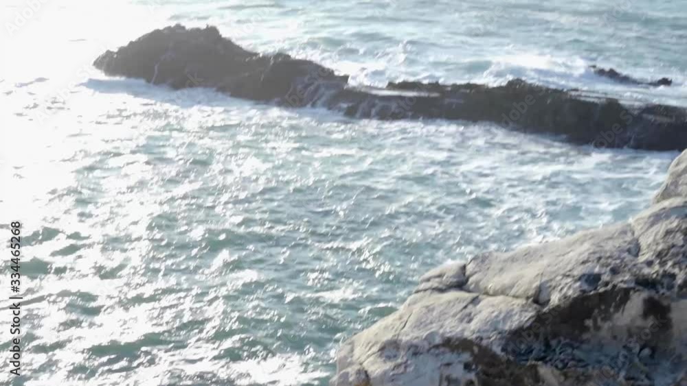 Moving backward from the view of waves crashing between rocks into above the ocean view. Moving backward from the view of waves crashing between rocks into above the ocean view.