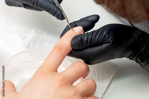 Beautician cutting cuticles of female nails during manicure procedure.