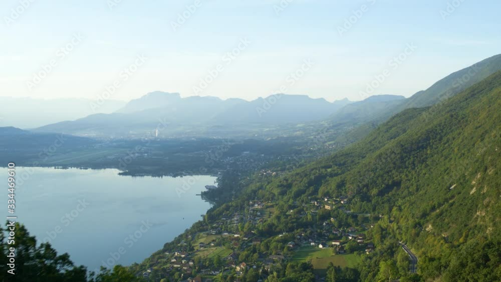 Aerial view of the mountain lake surrounded by the mountains covered in green forest with some houses by the coast in french alps. Aerial view of the mountain lake surrounded by the mountains covered in green forest with some houses by the coast in french alps.
