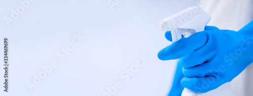 Fotografie Young woman housekeeper in apron is doing cleaning with blue gloves, wet yellow rag, spraying bottle cleaner, close up, copy space, blank design concept